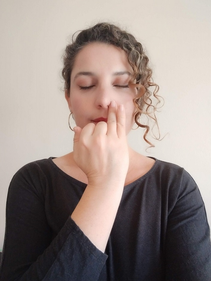 Mujer realizando ejercicio respiratorio con los ojos cerrados y tapando su narina izquierda con la mano derecha.